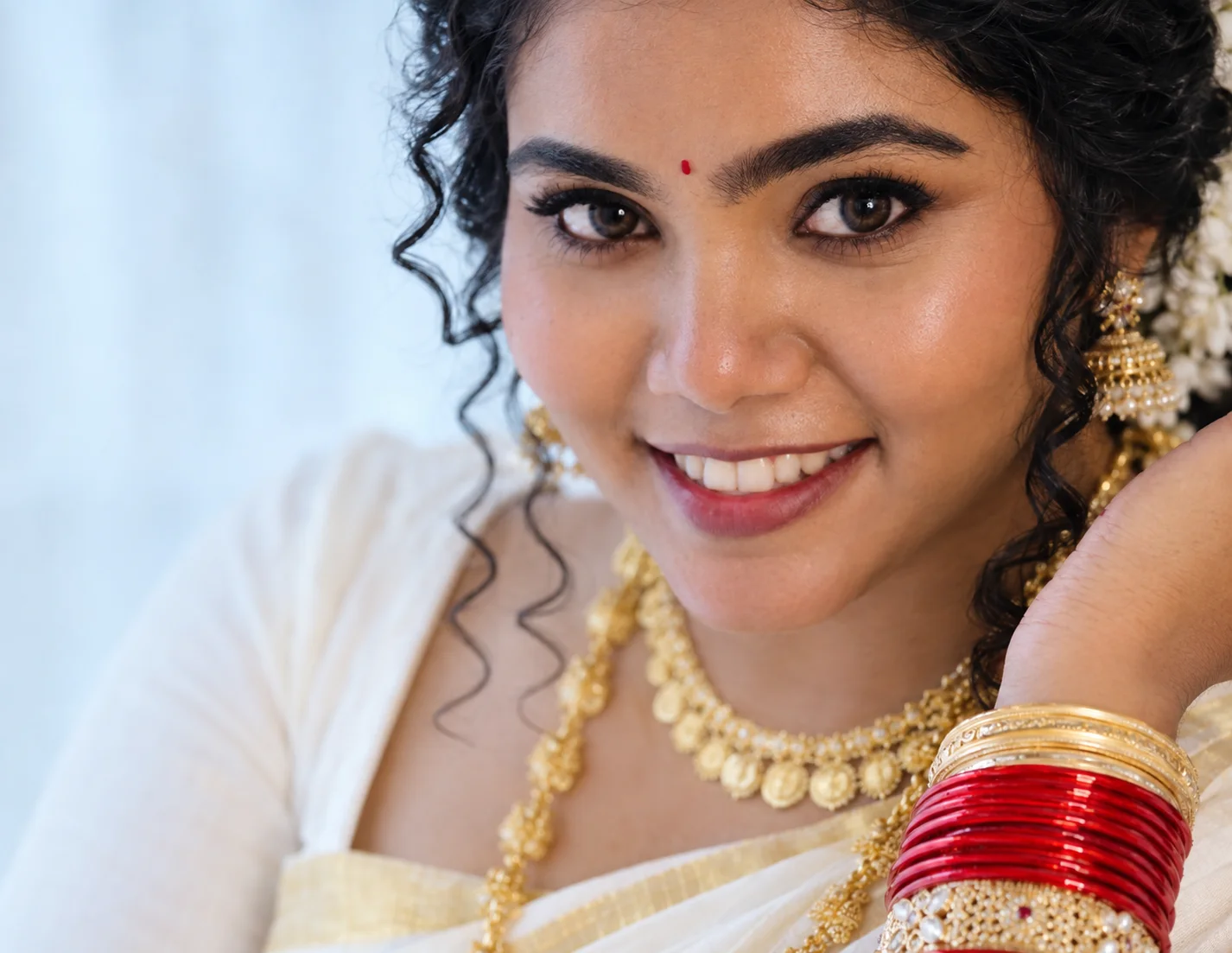 Bridal Makeup Guruvayur featuring a beautiful bride with elegant eye makeup, a traditional bindi, gold jewelry, and a radiant smile.